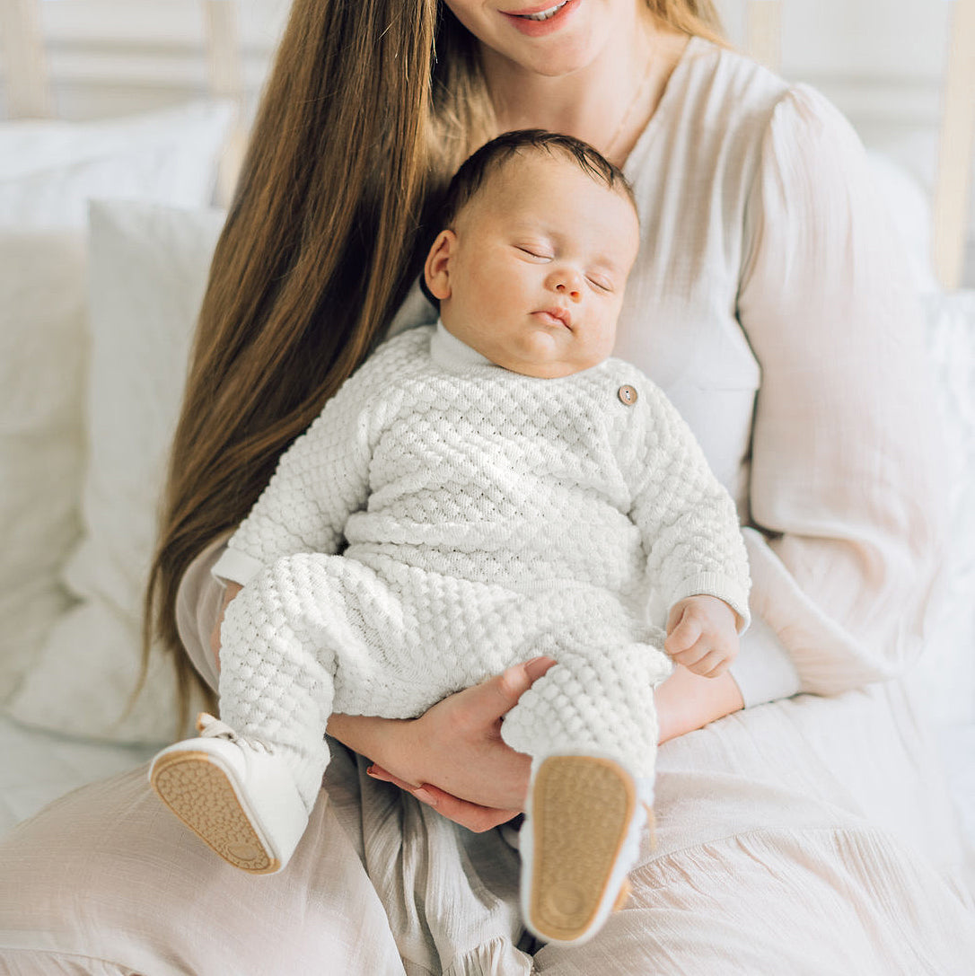 Baby sleeping on mom in William blessing outfit. 