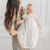 Baby in lace bonnet and long blessing dress siting in mothers arms.