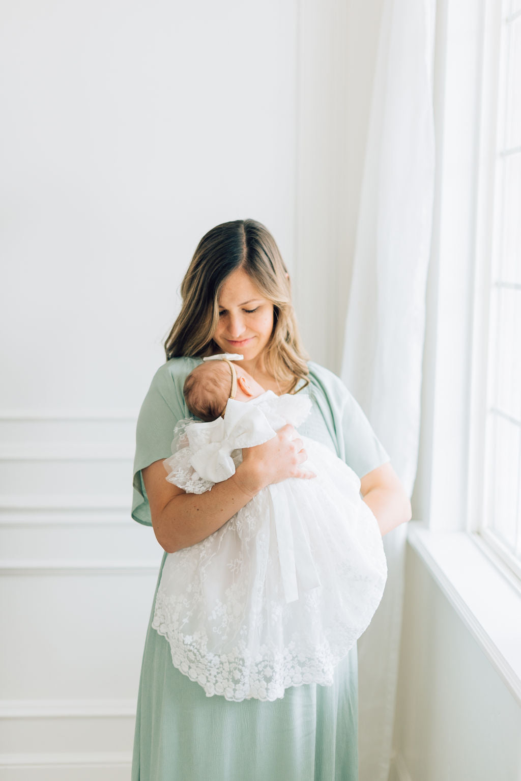 Baby laying on mother chest in arms in Eva Jane lace baby blessing dress with big bow in back