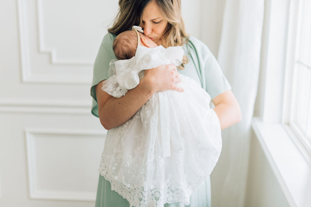 mom holding baby girl showing the back of blessing dress