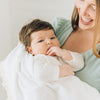 Baby boy sucking on fingers wrapped in white blanket with tassels.