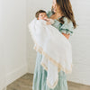 White blanket with cream tassels on edge wrapped around baby boy in mothers arms.