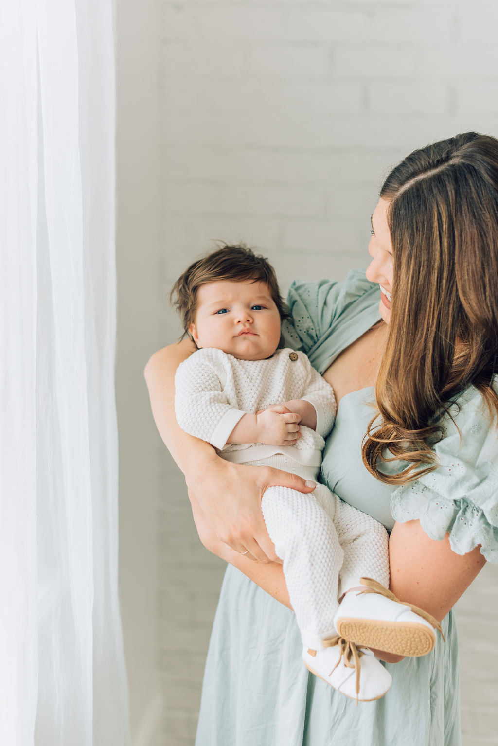 Baby boy in moms arms wearing the William baby blessing set with white shoes. 