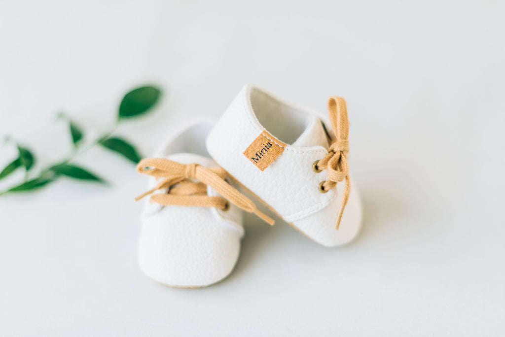 White baby boy shoes with brown laces with Miriia tag in brown