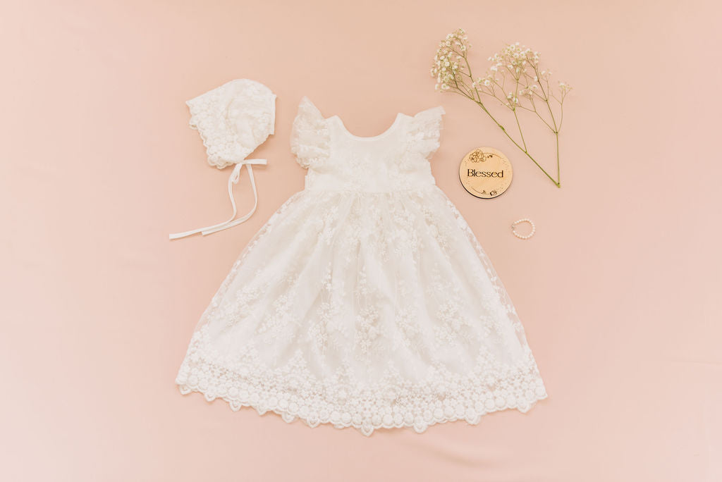 blessing christening dress flat lay with bonnet, photo prop, and pearl bracelet