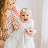 Baby smiling at camera in lace dress with simple white bow in mothers arms.