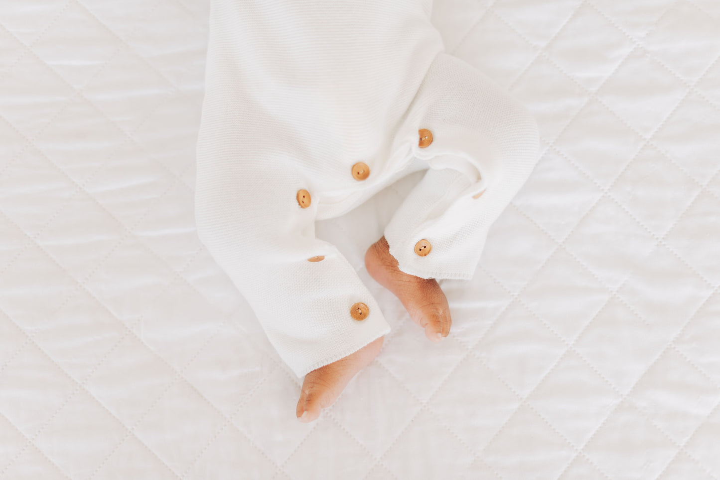 Detail shot of bron buttons on bottom of white baby boy blessing onesie. 