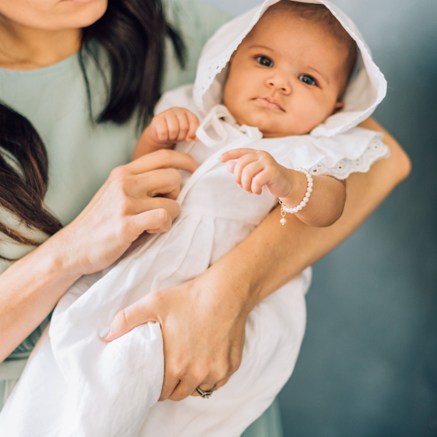 baby laying in mothers arms wearing pearl bracelet with white dress and bonnet